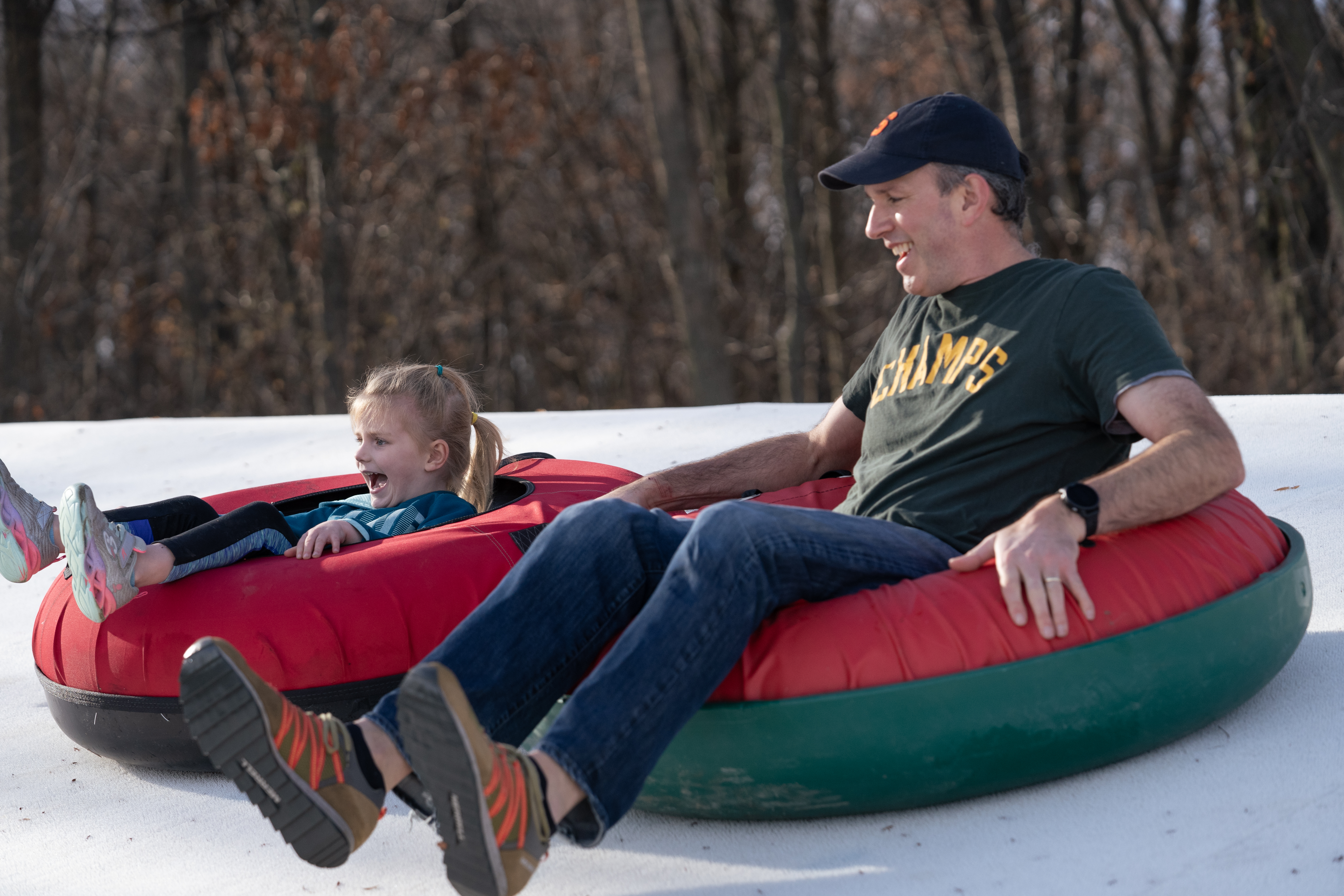 Parent and child on inner tubes sliding down a tubing hill.